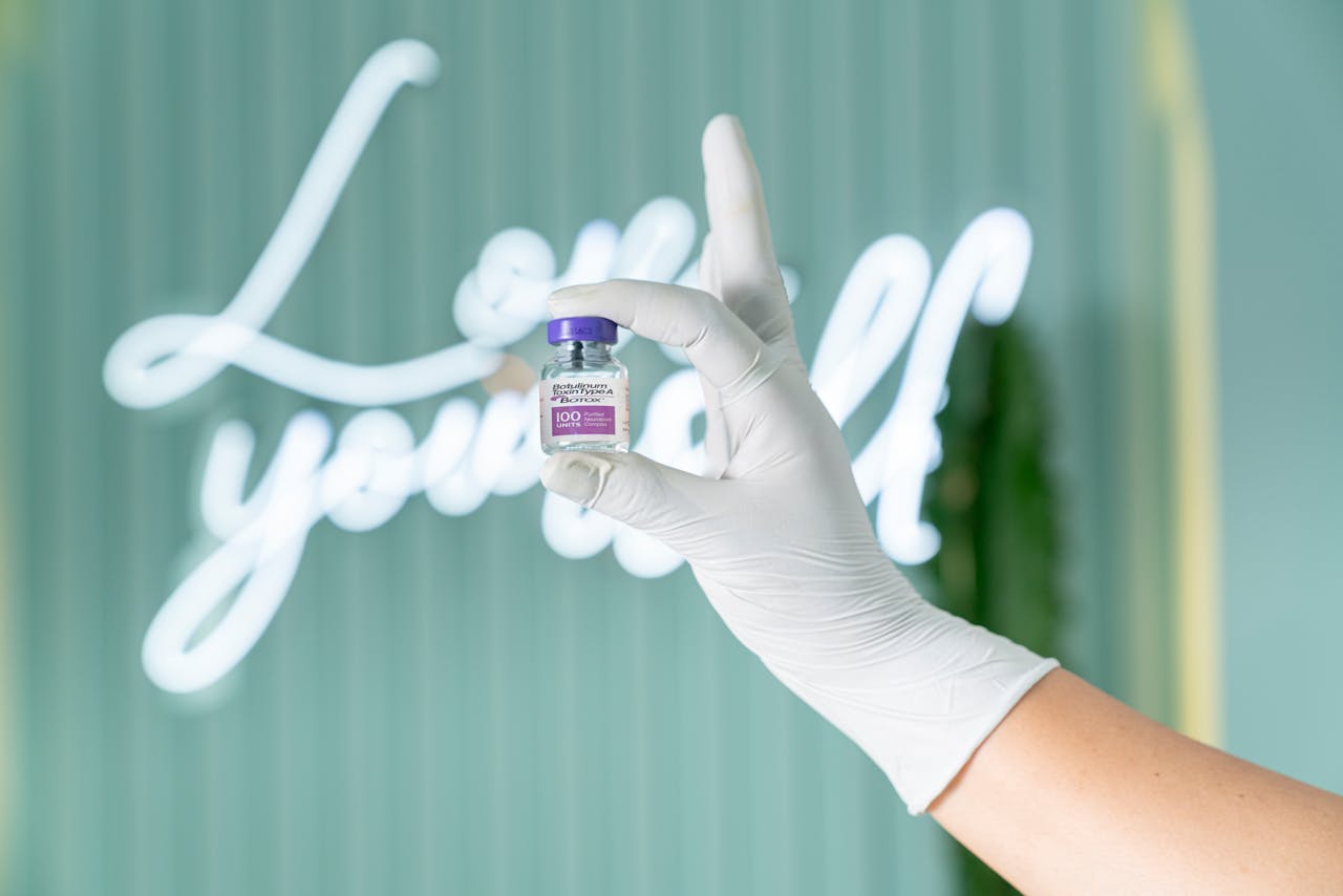 A gloved hand holds a Botox vial against a soft green background with neon lights.