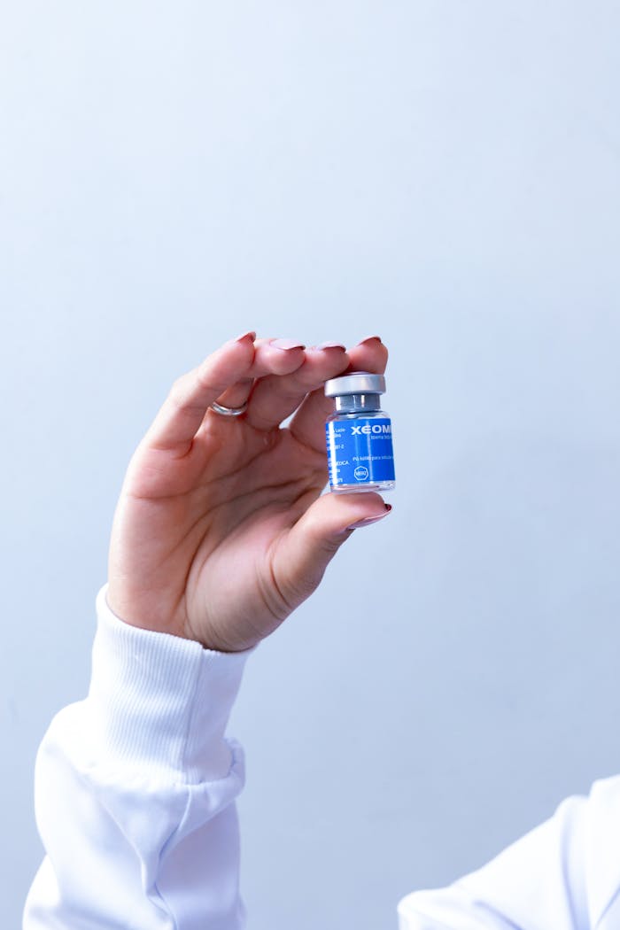 A woman's hand holding a small blue vial of cosmetic injectable product against a light background.