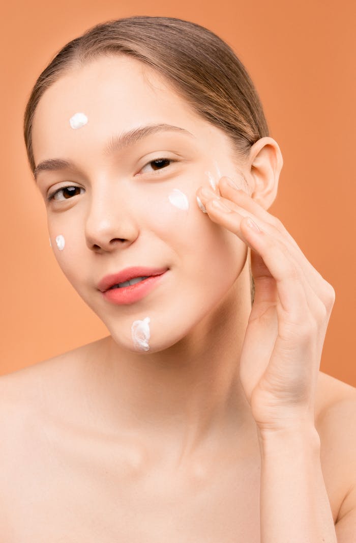 Close-up of a young woman applying facial moisturizer with a serene expression.