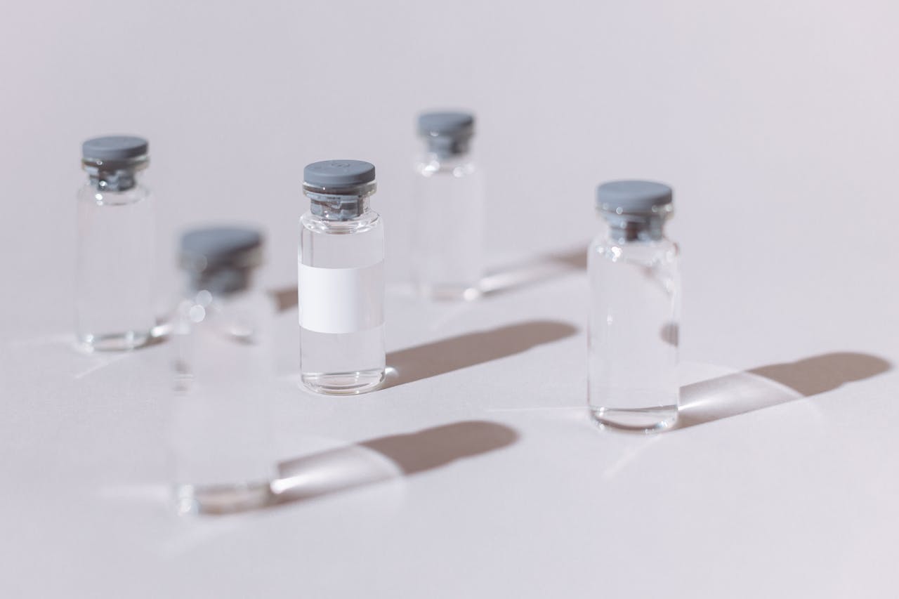 Clear glass vials used for vaccines or medication, displayed on a sterile white surface.