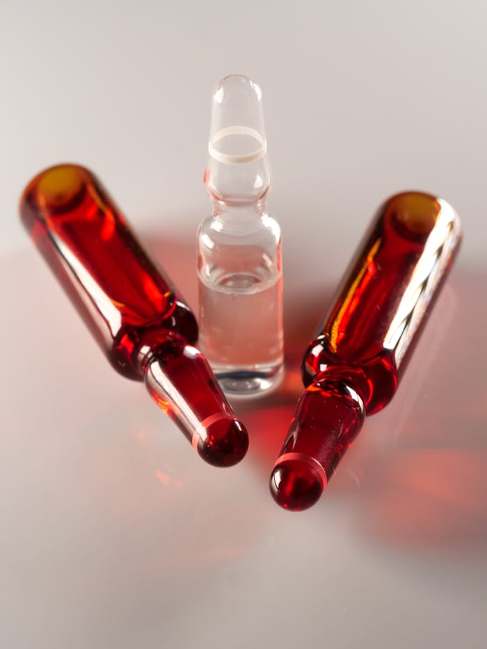 Three medical ampoules on a white surface, highlighting their red and clear glass design.